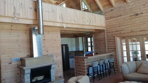 A wooden cabin interior with a fireplace, kitchen area, and seating. - Chalet de Charme (Al Arz)