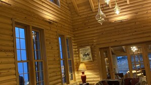 A log cabin interior with a large window, wooden ceiling beams, and a cozy seating area with a sofa and armchairs. - Chalet de Charme (Al Arz)