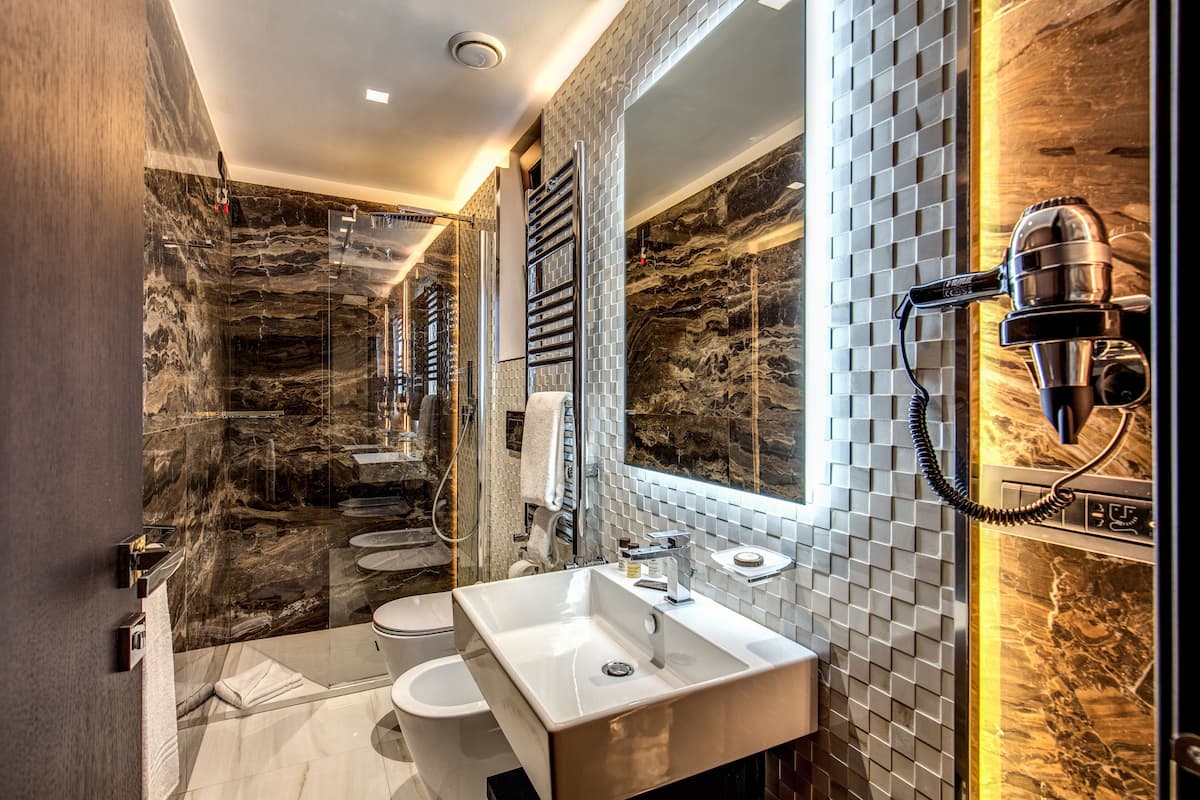A modern bathroom with a marble wall, a large mirror, a built-in sink, and a hairdryer mounted on the wall.