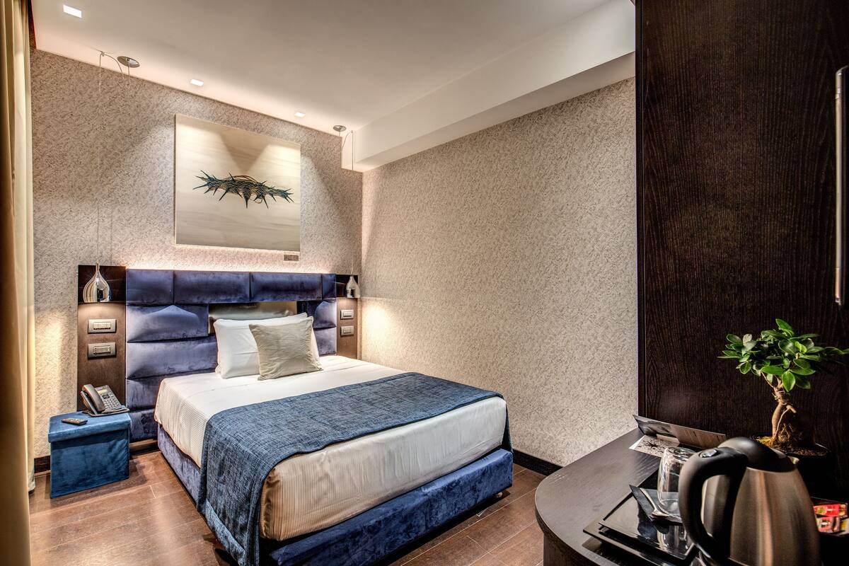 A modern bedroom with a large bed, a desk, and a potted plant.