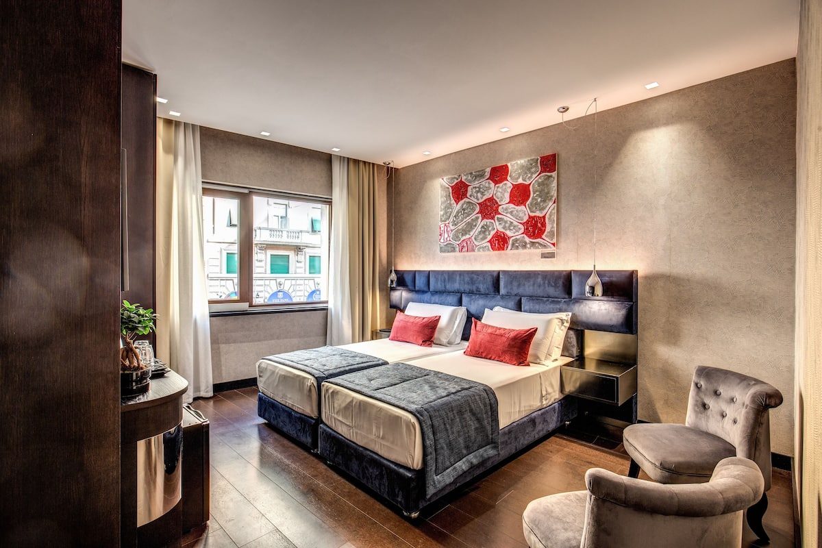 A modern bedroom with a large bed, a bedside table, a chair, and a window with curtains.