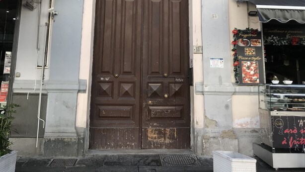A building with a large brown door, a small window, and a balcony with a railing. - Terrazza Carlo terzo (Naples)