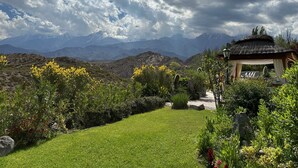 Un jardín con un pabellón, un espacio cubierto de césped y montañas al fondo.