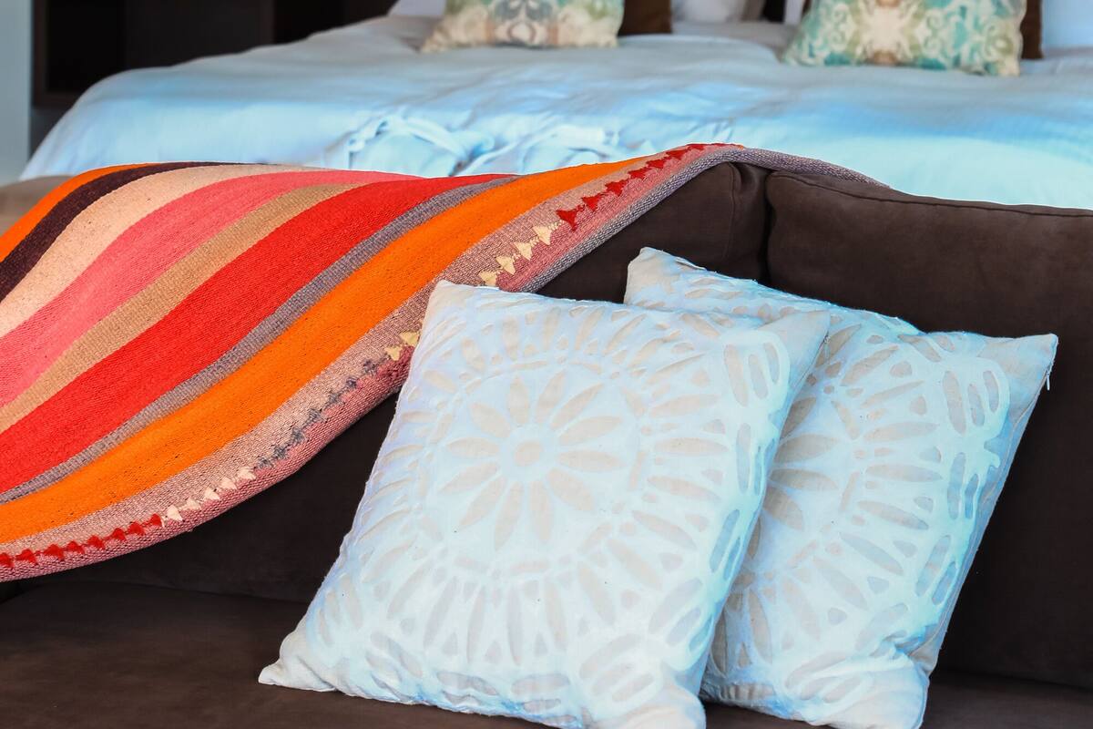 Un dormitorio con una cama, almohadas, una colcha, una mesita de noche y un cuadro en la pared.