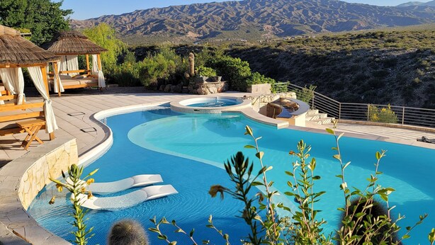 A swimming pool with a curved design, surrounded by a stone deck and wooden loungers. - El Carmelo Mountain Lodge (Potrerillos)