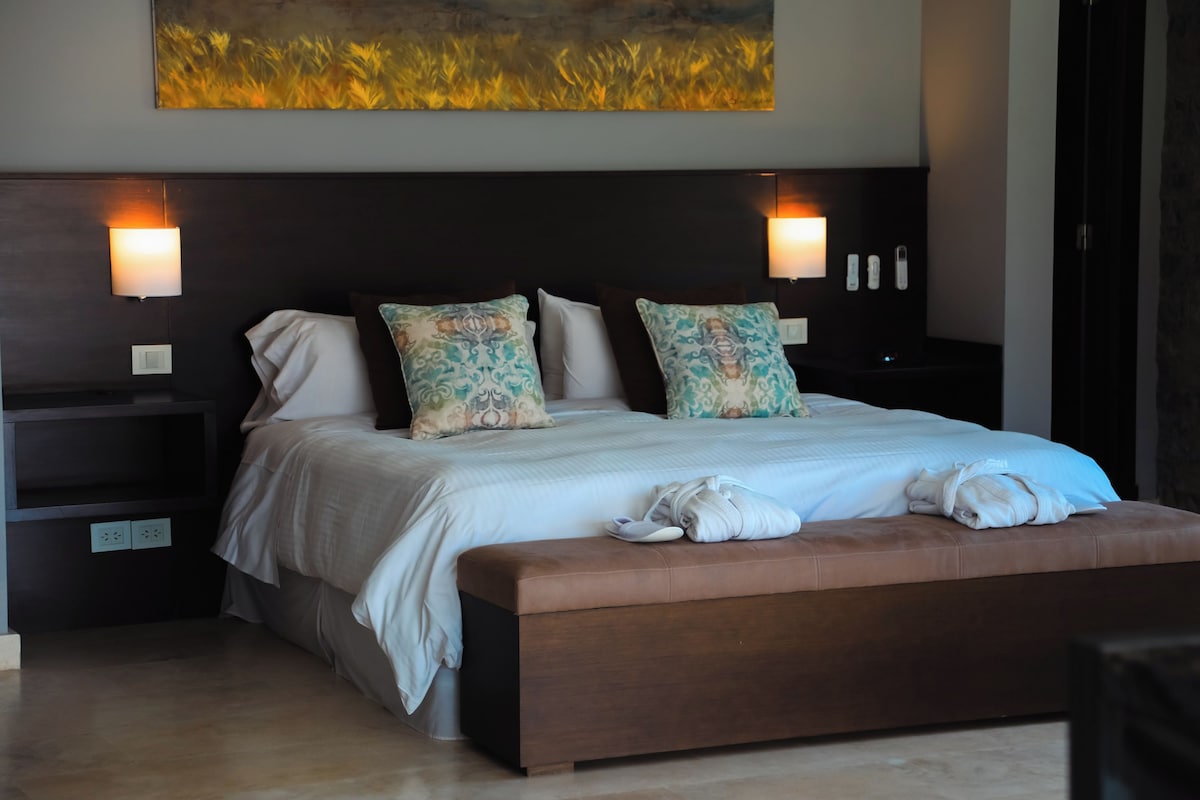 A modern bedroom with a large bed, two bedside tables, and a headboard with wall-mounted lights.