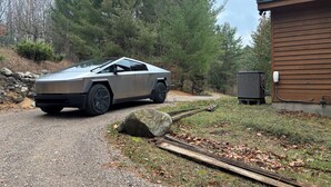 Un véhicule futuriste est garé sur un chemin de gravier, près d’un bâtiment en bois équipé d’un climatiseur.