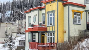 A multi-story building with a yellow facade, red accents, and a balcony. - Bright, upgraded townhouse in Creekside w/laundry, hot tub, close to village (Silver Star Mountain)