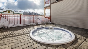 Et spabad i et udendørs område med flisegulv, omgivet af et rødt hegn, og en bygning med balkon i baggrunden.