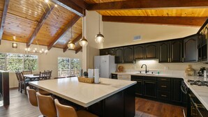 A spacious kitchen with a large island, dark cabinetry, and a wooden ceiling. - Bare Necessities - AC, Hot Tub, Pool Table, and Lake Views! Walking distance to the Village. (Big Bear Lake)