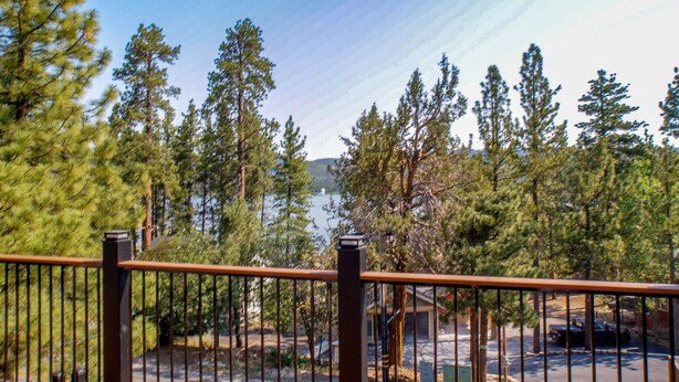 A view from a balcony with a metal railing, overlooking a parking area with cars and a building in the background. - Bare Necessities - AC, Hot Tub, Pool Table, and Lake Views! Walking distance to the Village. (Big Bear Lake)
