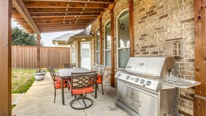 Un patio cubierto con pared de ladrillo, una parrilla y una mesa con sillas.