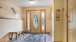 Un couloir avec un banc, un tapis à motifs et une porte à panneaux de verre.