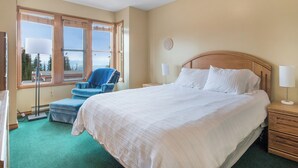 Une chambre d’hôtel avec un grand lit, une chaise, une table de chevet et une fenêtre donnant sur un beau paysage.