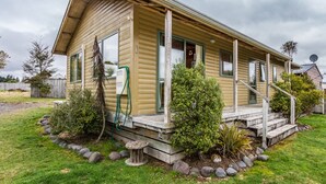 Une maison mobile de plain-pied, dotée d’un porche, d’une antenne parabolique et d’un jardin agrémenté de rochers et d’arbustes.