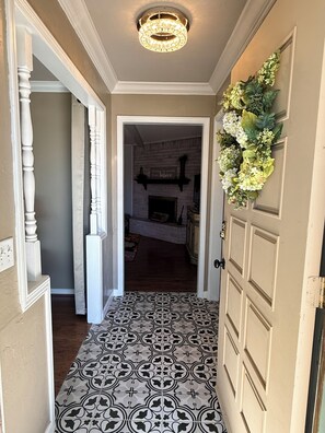A hallway with patterned flooring, a chandelier, and a decorative wall hanging.