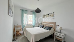 A bedroom with a bed, a nightstand, a lamp, a window with curtains, and a hanging light fixture.