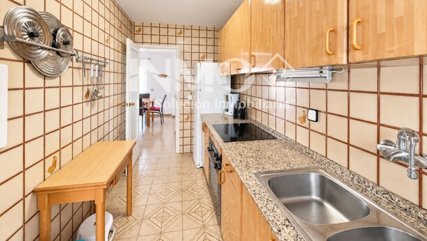 Una cocina con armarios de madera, encimera de granito, un lavamanos y un comedor visible al fondo.