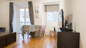 Una habitación con suelo de madera, una mesa de comedor con sillas, un televisor y un escritorio.