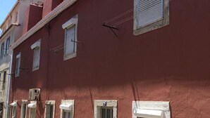 Una hilera de edificios rojos con numerosas ventanas y puertas, algunas con contraventanas, y un cielo despejado al fondo.