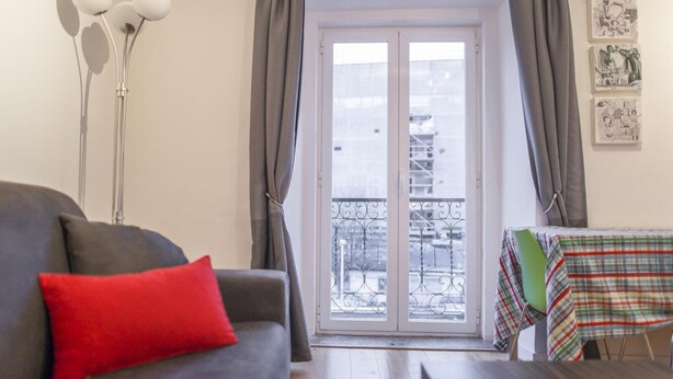 Una sala de estar con un sofá gris, un cojín rojo y una mesa con mantel a cuadros.