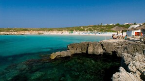 Een kuststrand met helder turquoise water, rotsformaties en enkele strandparasols.