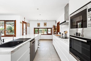 A modern kitchen with a large island, built-in oven, and a view of the outdoors. - VILLA PARIS IN BINIBECA NOU | Sunsets, Luxury and Family Security (Sant Lluis)