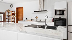 Een moderne keuken met een marmeren aanrecht, roestvrijstalen apparatuur en houten planken.