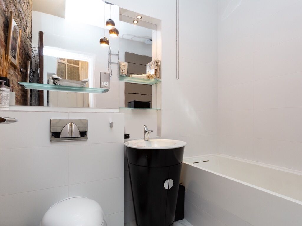 Un baño moderno con un lavamanos blanco, un cubo de basura negro y un estante de vidrio.