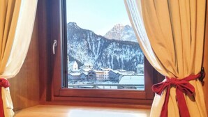 A window with curtains tied back, revealing a snowy mountain view.