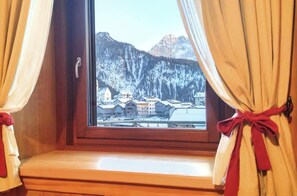Une fenêtre dont les rideaux sont attachés, laissant apparaître un paysage montagneux enneigé avec des bâtiments.