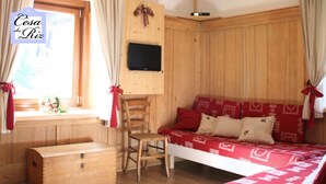 A cozy room with a wooden bed, a wooden chest, and a chair. A flat-screen TV is mounted on the wall.