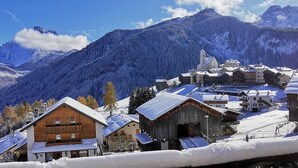 A snow-covered village with traditional wooden buildings and a church, surrounded by mountains.
