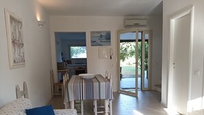 A living room with a sofa, a dining table with chairs, and a kitchen area visible through an open door.