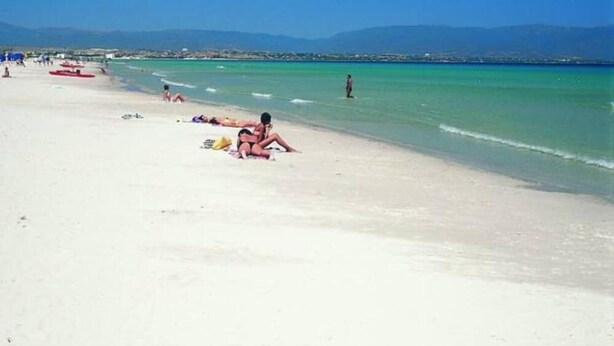 A beach with people sunbathing and swimming.