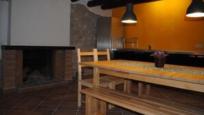 Un rincón comedor acogedor con chimenea de ladrillo, mesa y bancos de madera, e iluminación colgante.