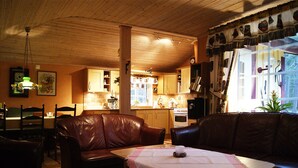 A cozy living room with a brown leather sofa, a wooden dining table with a pink tablecloth, and a kitchen in the background. - Lovely cottage in Juleboda, close to the sea with wonderful sandy beach (Degeberga)