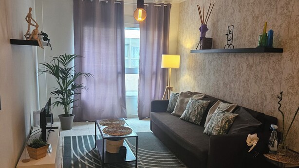 A living room with a sofa, a coffee table, a lamp, a plant, and a view of the outdoors through curtains. - Exposito's Vacation Home  (Las Palmas de Gran Canaria)
