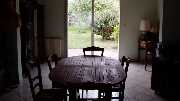 A dining area with a round wooden table and chairs, a cabinet, a radiator, and a view of the backyard through a glass door. - Recent villa in quiet traditional neighborhood (Andernos-Les-Bains)