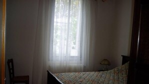 A bedroom with a bed, a chair, a window with sheer curtains, and a bedside lamp. - Recent villa in quiet traditional neighborhood (Andernos-Les-Bains)