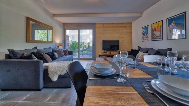 Una sala de estar moderna con un sofá, una mesa de comedor lista para cuatro personas y un televisor al fondo.