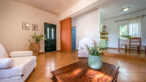 A living room with a sofa, a wooden coffee table, a green door, and a dining area with a chair and table.