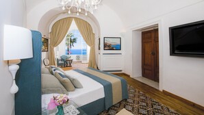 A bedroom with a bed, a chandelier, a TV, and a view of the sea through a window. - AMORE RENTALS - Villa Mimosa with Private Pool, Sea View, Air Conditioning, Positano Center (Positano)