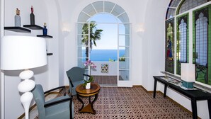 A room with a view of the ocean, a chair, a table with a vase of flowers, and a lamp. - AMORE RENTALS - Villa Mimosa with Private Pool, Sea View, Air Conditioning, Positano Center (Positano)