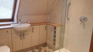 Een moderne badkamer met een wit wastafelmeubel, beige kastjes, een douchecabine met glazen wanden en een raam met zonwering.