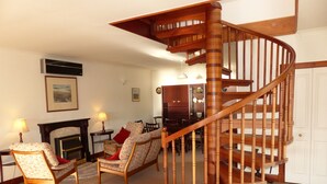 Un salón amplio con una escalera espiral de madera, una chimenea y asientos cómodos.