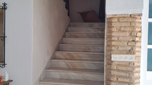 A marble staircase leading to an upper floor, with a brick column and a potted plant at the bottom. - Apartment in Historic Sanluqueña House With Charm (Sanlúcar de Barrameda)
