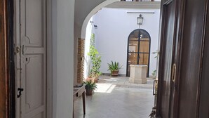 An arched corridor with a tiled floor, a wooden door on the right, and a white door on the left. - Apartment in Historic Sanluqueña House With Charm (Sanlúcar de Barrameda)