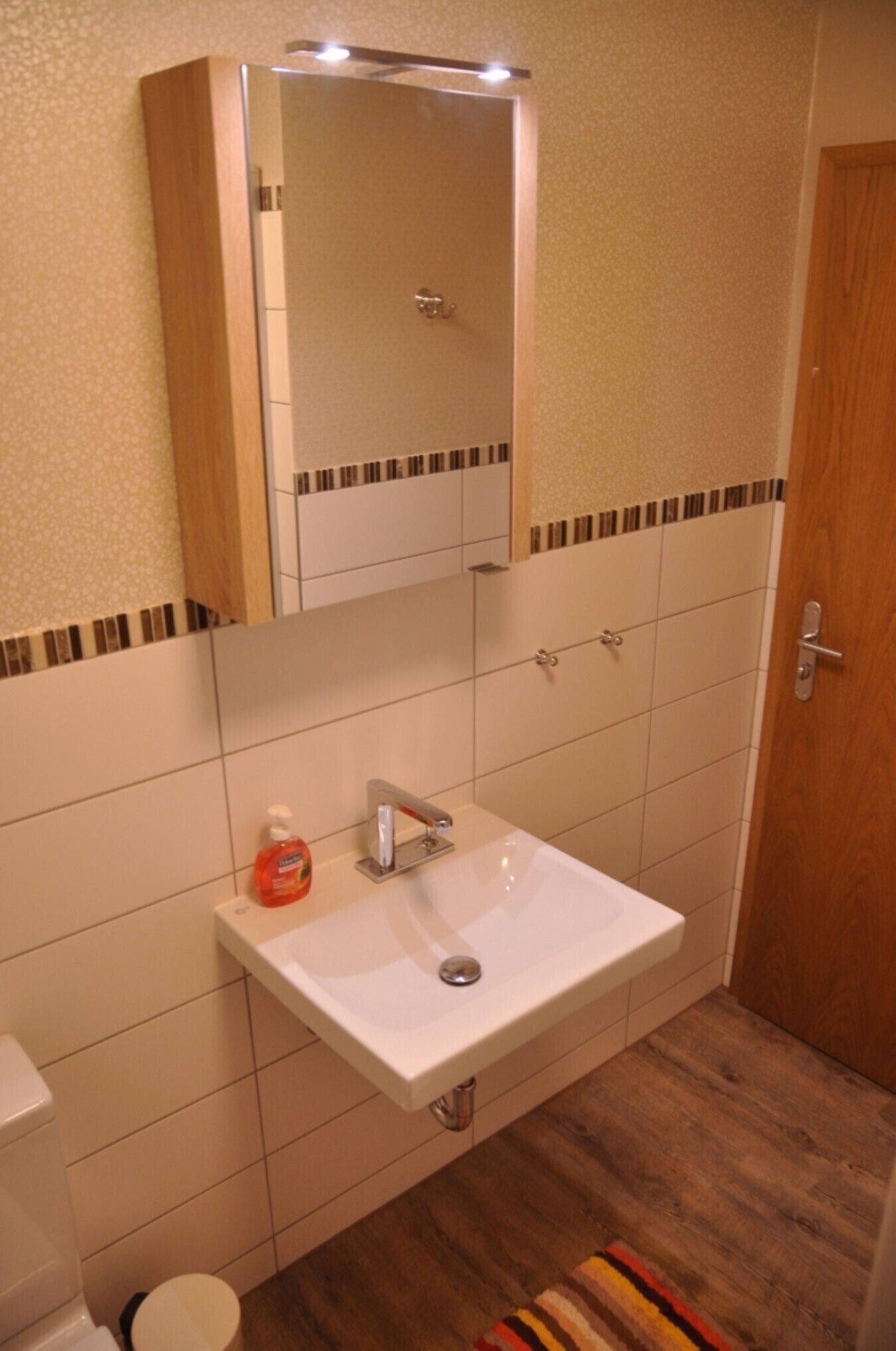 A bathroom with a white sink, a mirror above it, and a wooden door.