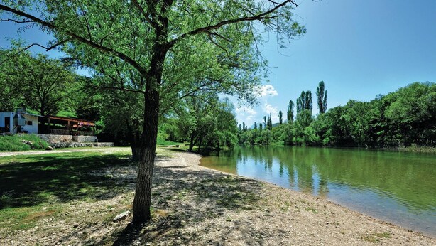 Une vue sur la rivière, avec un bâtiment sur la gauche, un chemin de gravier et des arbres le long de la rive.
